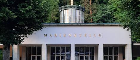 A building with the name 'MARIE NQUELLE' on the facade, featuring a central column, large windows, and two benches in front.