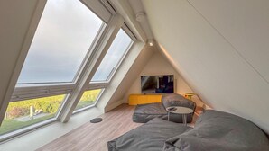 A modern loft bedroom with large skylights, a flat-screen TV, and a cozy seating area. - Wellness villa with sauna, garden and sea nearby (Colijnsplaat)