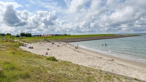 A beach with a sandy shore, grassy areas, and a calm sea. - Wellness villa with sauna, garden and sea nearby (Colijnsplaat)