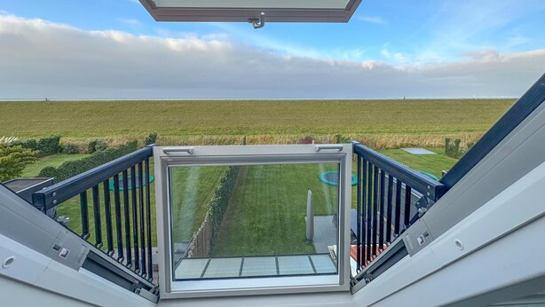 A balcony with a glass enclosure overlooking a grassy field and a clear sky. - Wellness villa with sauna, garden and sea nearby (Colijnsplaat)