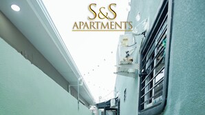 A narrow alleyway with a gravel path, flanked by light green walls and a window with a metal grill. - S&S APARTMENT #1 .3 MTS FROM FERRY (La Ceiba)