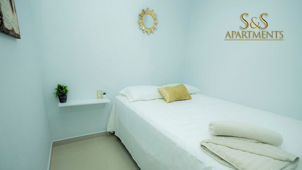 A bedroom with a bed, a nightstand, a small shelf with a plant, and a wall decoration. - S&S APARTMENT #1 .3 MTS FROM FERRY (La Ceiba)