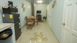 A compact kitchen with a microwave, refrigerator, and a stove. There is a dining area with a table and chairs. The walls are light-colored, and there is a door on the right. - S&S APARTMENT #1 .3 MTS FROM FERRY (La Ceiba)