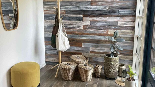 Un intérieur moderne avec un mur en bois, un pouf jaune, des paniers tress és et une plante en pot.