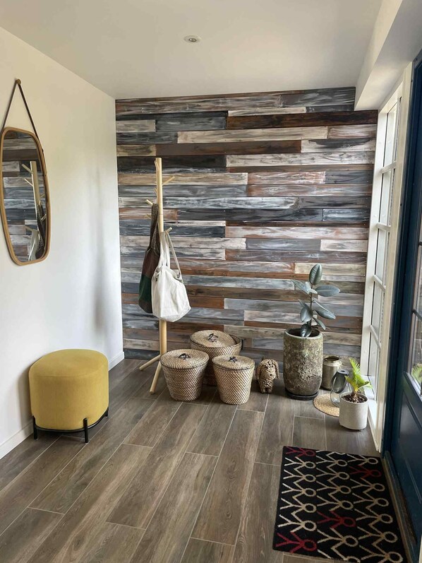Ein modernes Interieur mit einer Holzwand, einem gelben Ottomanen, gewebten Körben und einer Topfpflanze.