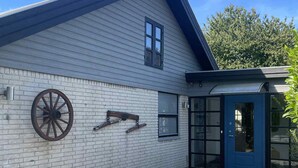 Un bâtiment à l’extérieur en briques blanches, avec une porte bleue et une grande décoration en forme de roue sur le mur.