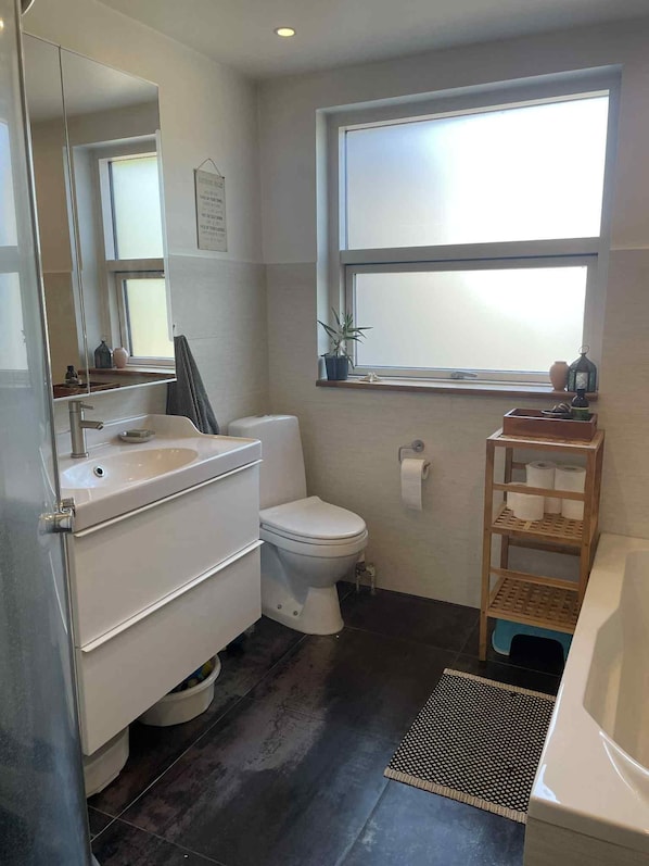 A modern bathroom with a white toilet, a sink, a mirror, a window, and a shelf with toiletries.