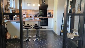 Une cuisine moderne dotée d’un îlot central, d’un revêtement de sol en carrelage noir et offrant une vue sur la salle à manger grâce à une cloison en verre.