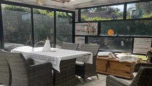 Une terrasse extérieure avec des meubles en osier, une table recouverte d’une nappe blanche et un coffre en bois.