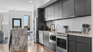 A modern kitchen with dark cabinets, stainless steel appliances, and a marble island. - NEW! 1mi->Broadway! Top of the Tune Penthouse (Nashville)