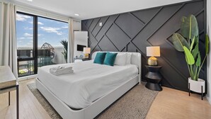 A modern bedroom with a large bed, a view through a sliding glass door, and a geometric wall design. - NEW! 1mi->Broadway! Top of the Tune Penthouse (Nashville)