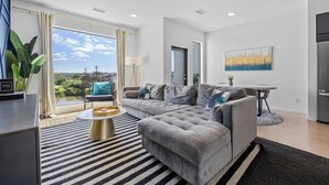 A modern living room with a grey sofa, a striped rug, and a view of greenery through large windows. - NEW! 1mi->Broadway! Top of the Tune Penthouse (Nashville)