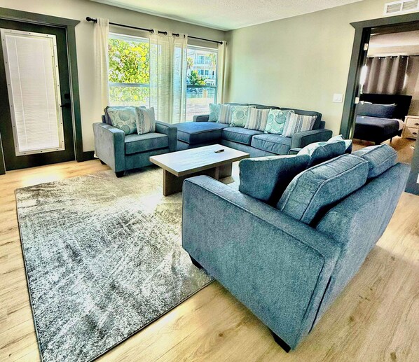 En moderne stue med en hjørnesofa, et sofabord og et stort vindue med gardiner.