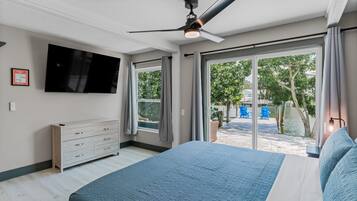A bedroom with a bed, a ceiling fan, a TV, and a view of a water body and greenery outside.