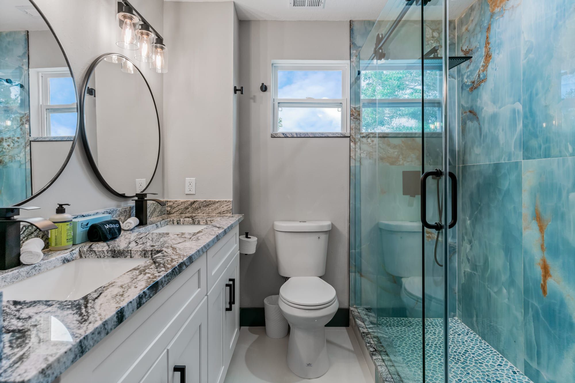 Un baño con encimera de mármol, inodoro, cabina de ducha de vidrio y un espejo grande con iluminación.