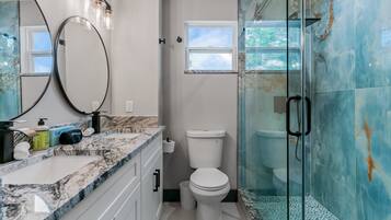 Un baño con encimera de mármol, inodoro, cabina de ducha de vidrio y un espejo grande con iluminación.