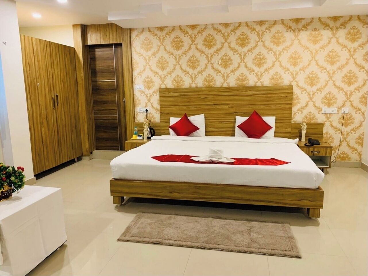 Een slaapkamer met een houten bed, wit beddengoed, rode kussens, een nachtkastje en een bedtafel.