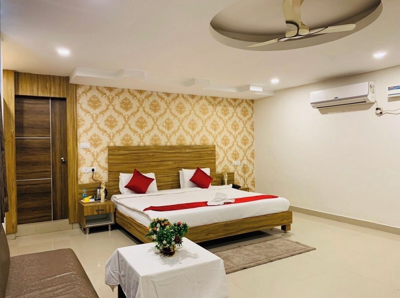 Een hotelkamer met een houten bed, een nachtkastje, een tafel met een bloevas en een airconditioning aan de muur.