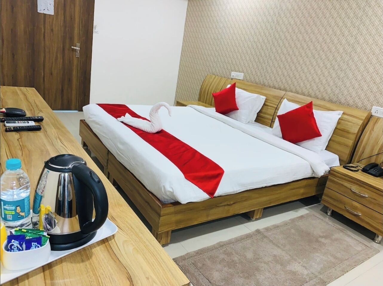 Une chambre d’hôtel avec un lit en bois, une table de chevet avec une bouilloire, une bouteille d’eau et une tasse de thé.