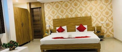 A hotel room with a wooden bed, red pillows, a small bedside table with a plant, and a patterned wallpaper.