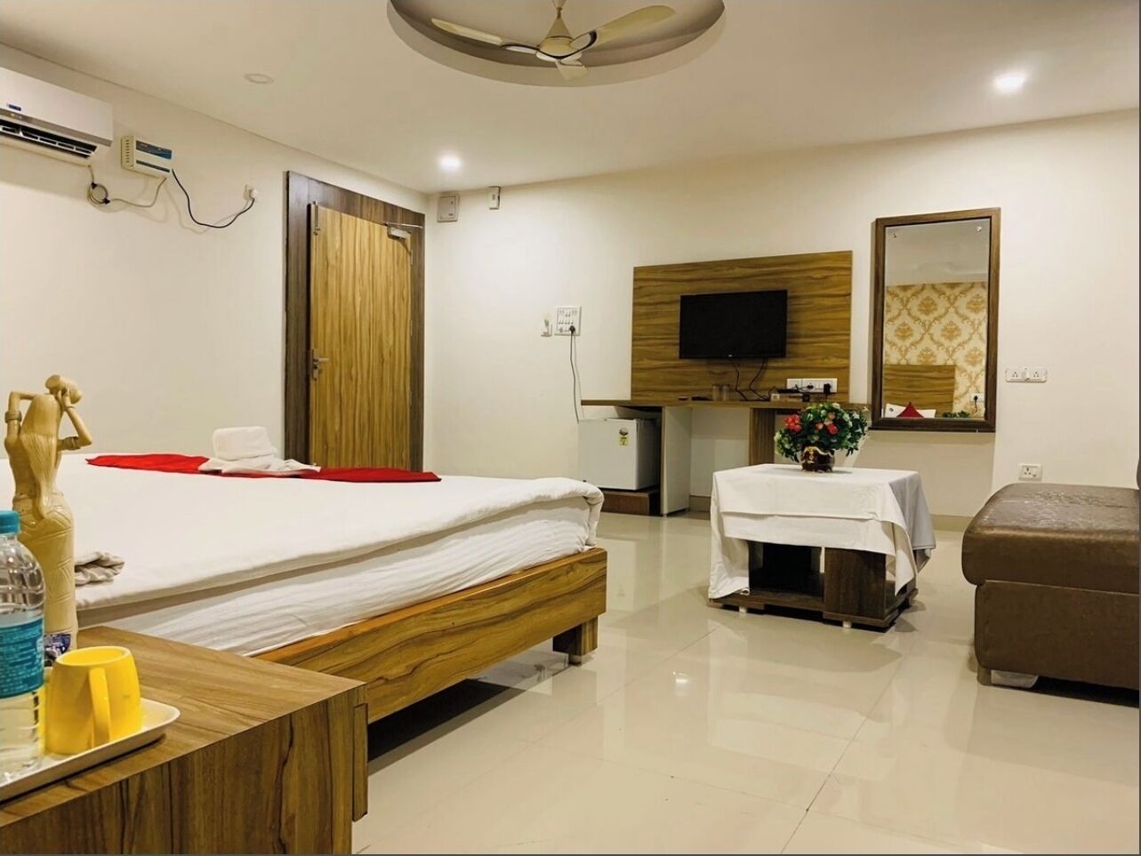 Una habitación de hotel con cama, una mesita con un florero, un sofá, un televisor y un armario de madera.