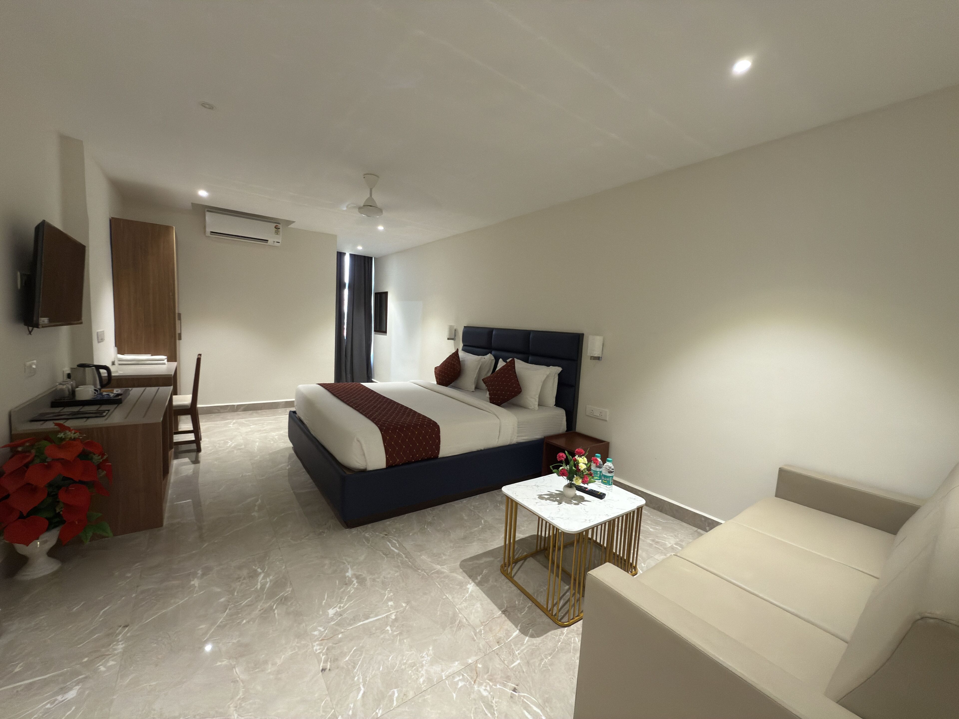 A modern hotel room with a bed, a desk, a chair, a small table, and a sofa.