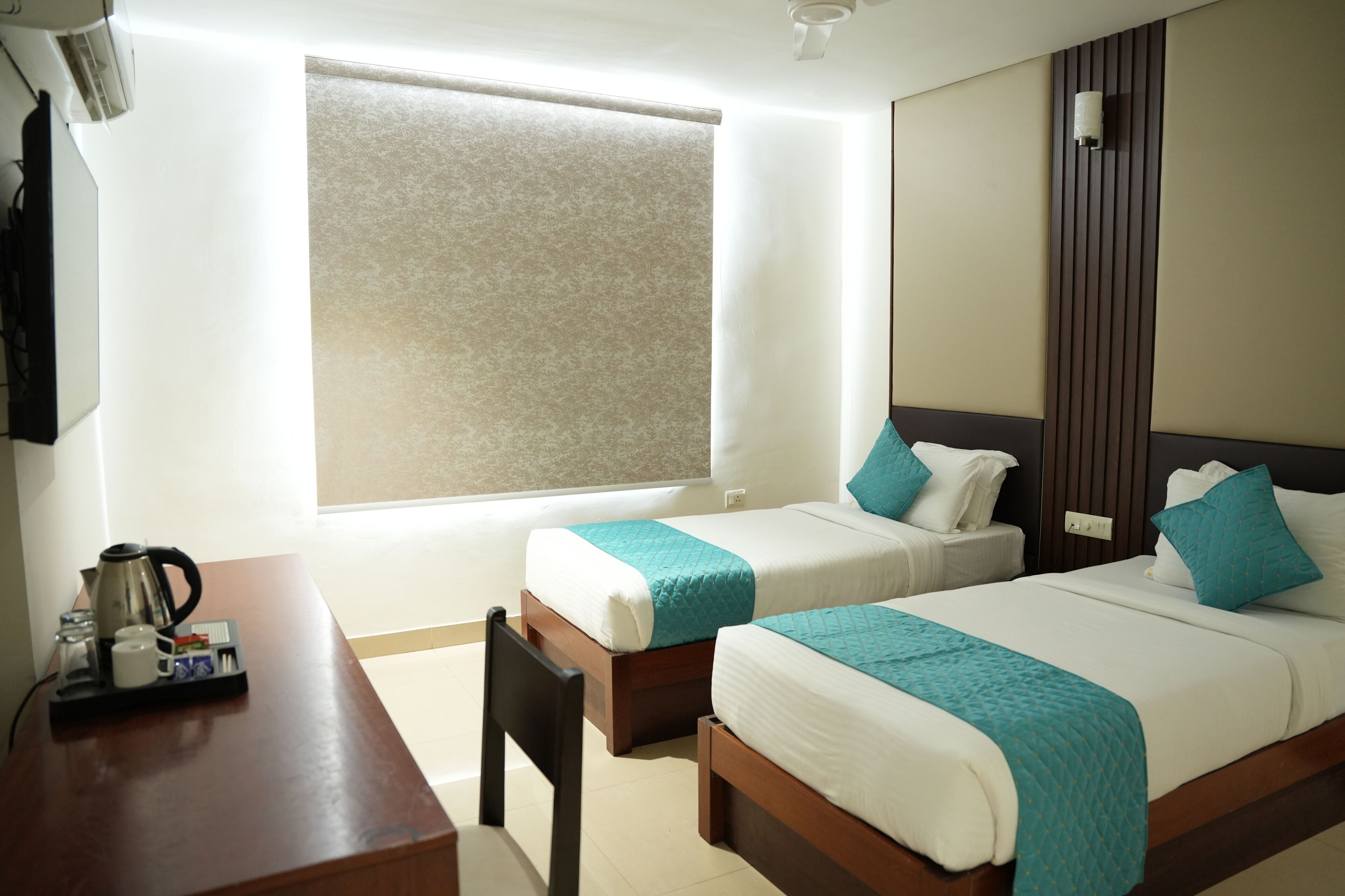 A hotel room with two beds, a desk with a coffee maker, and a large window.