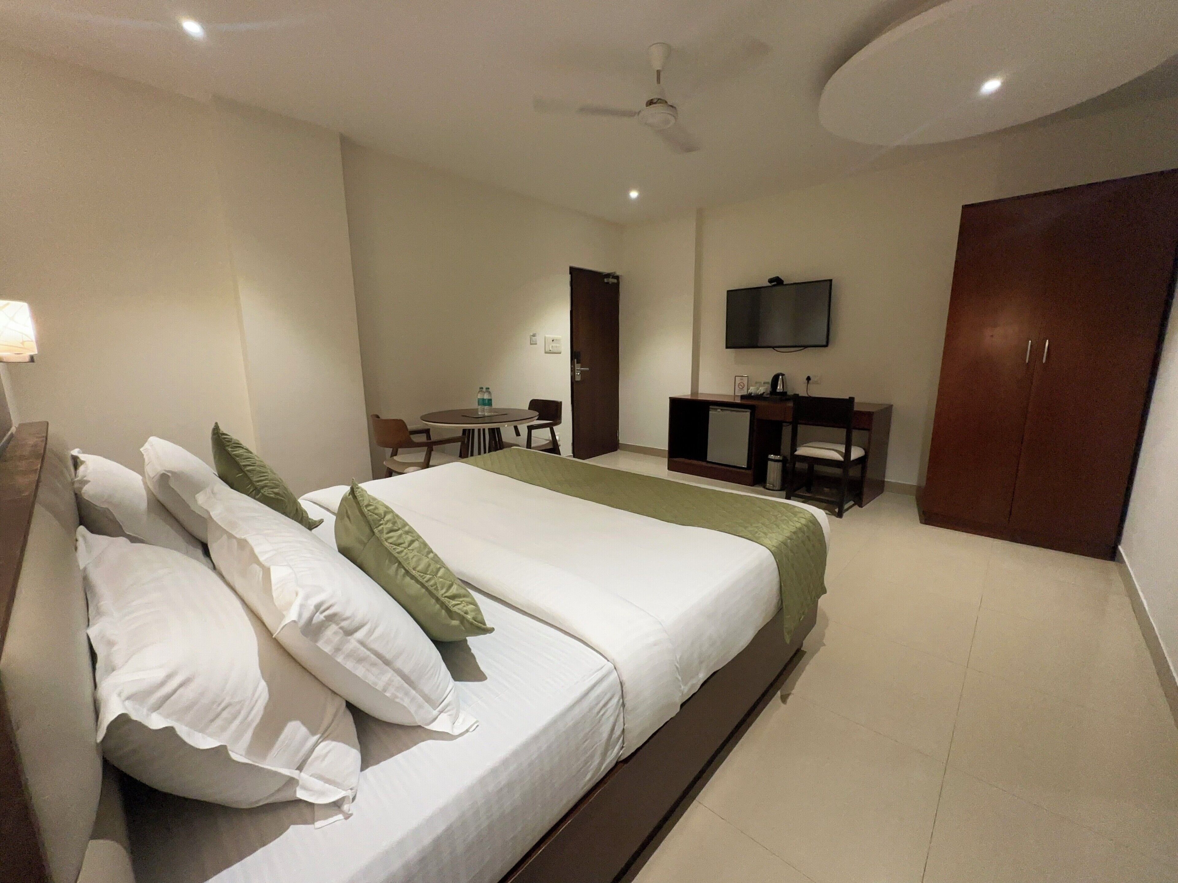 Una habitación de hotel con cama, escritorio, silla, televisor y armario.