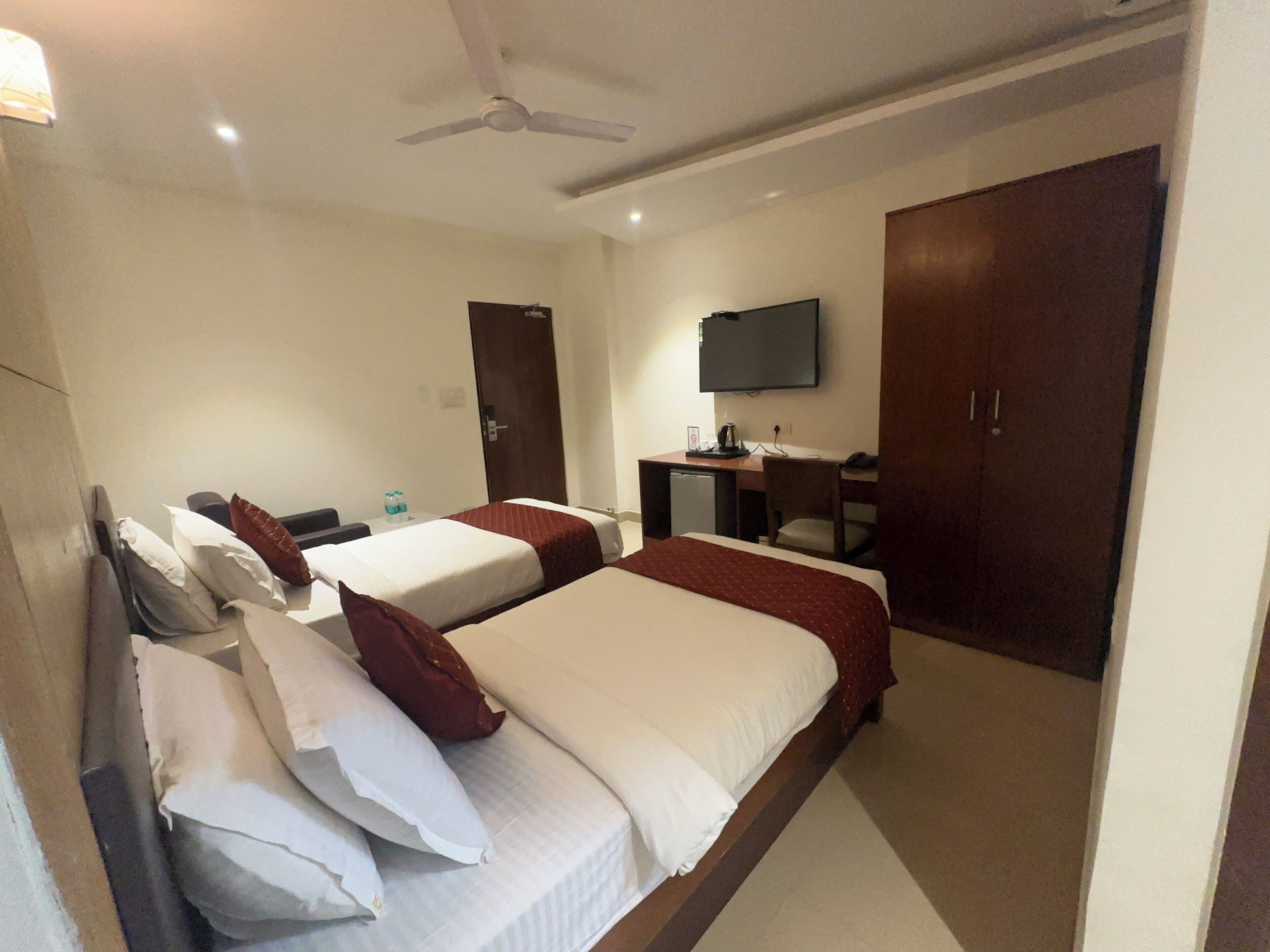A hotel room with two beds, a desk with a chair, a television, and a wardrobe.