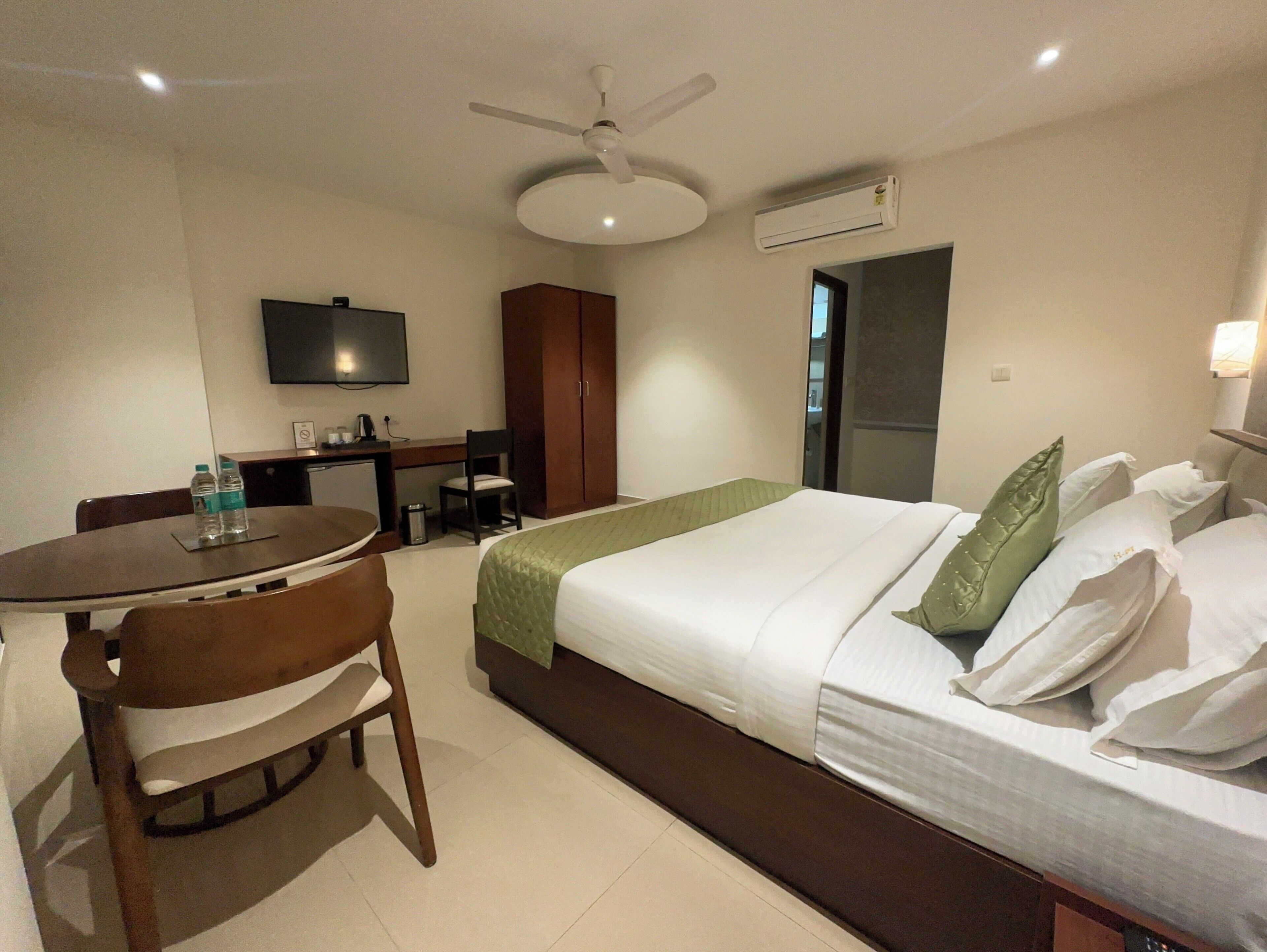 A hotel room with a bed, a desk, a chair, a television, and an air conditioning unit.