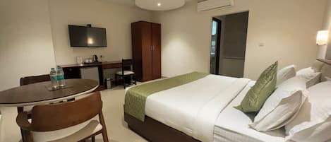 A hotel room with a bed, a desk, a chair, a television, and an air conditioning unit.