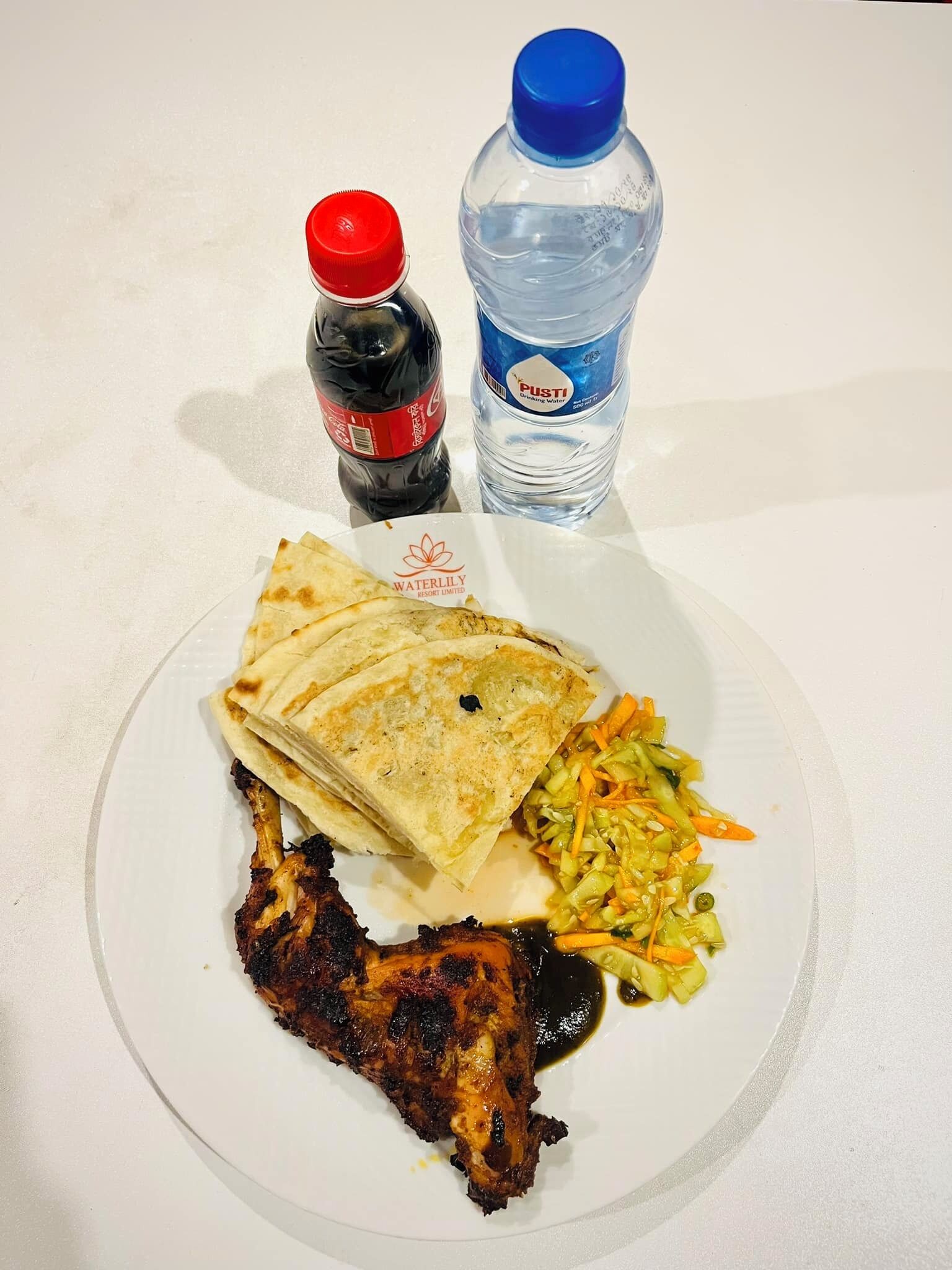 A plate with grilled chicken, flatbread, and a vegetable salad. There are two bottles of beverages, one red and one blue, on the table.