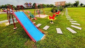 A playground with a blue slide, red swings, and red rocking horses.