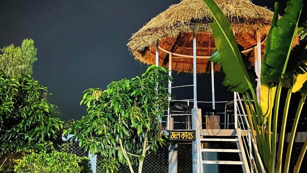 A gazebo with a thatched roof, surrounded by lush greenery and a staircase leading up to it.