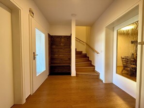 A hallway with wooden flooring, a wooden staircase, and white walls.
