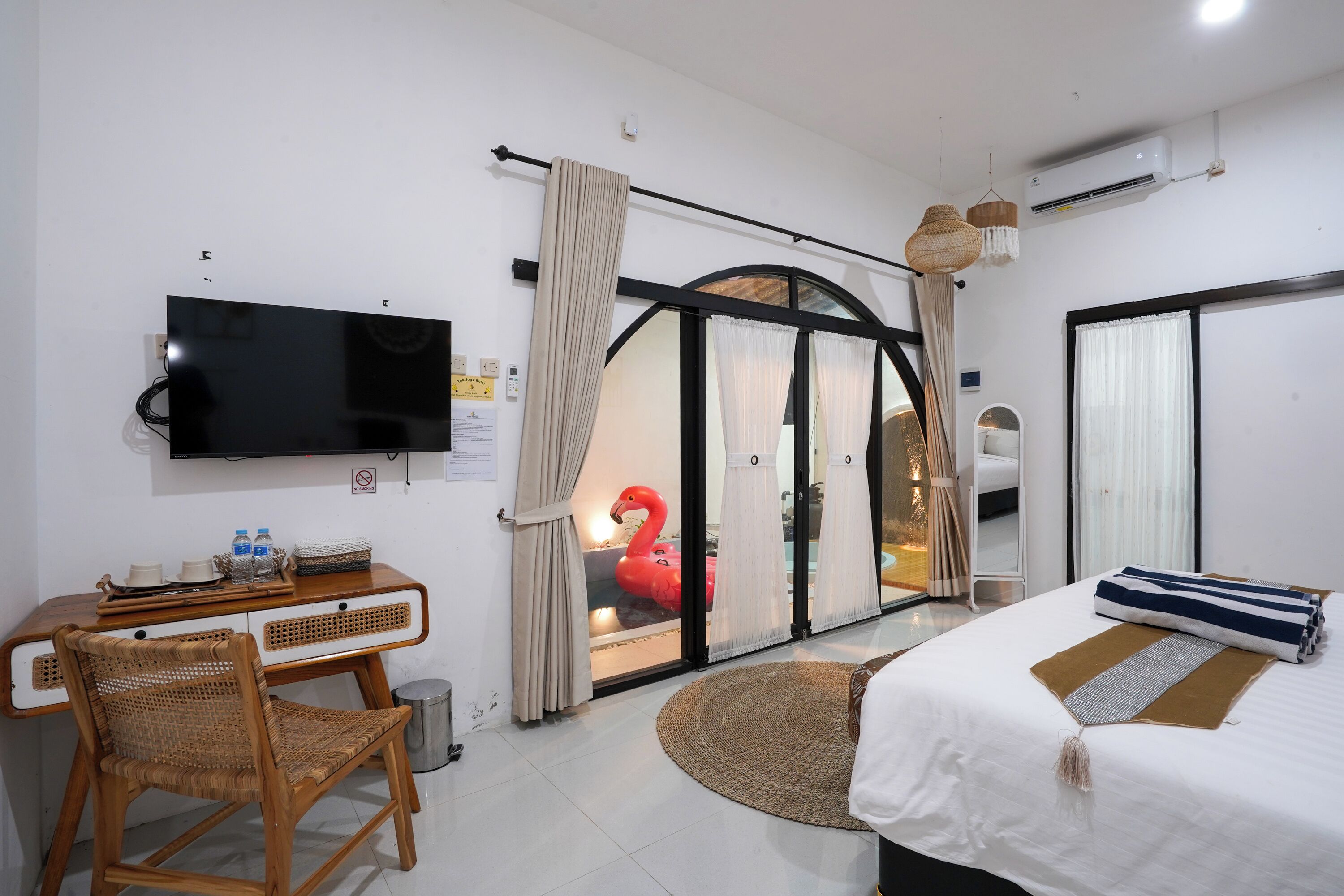A hotel room with a bed, a desk with a chair, a television, and a window with curtains.