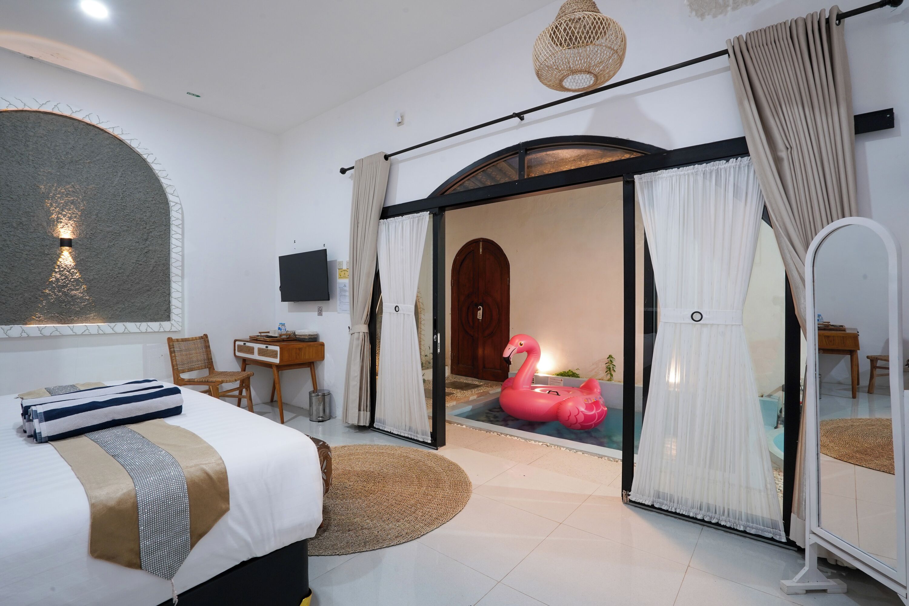 Ein Hotelzimmer mit Bett, Schreibtisch, Stuhl, Fernseher, Spiegel und einer Tür zu einem Badezimmer mit Flamingo-Dekoration.