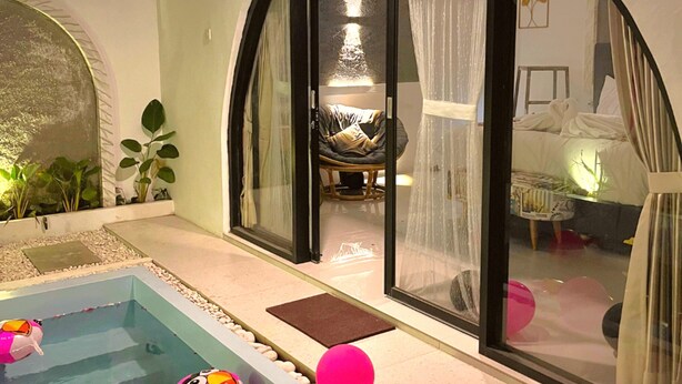 A pool area with a glass-enclosed room, a bed, and a dining area visible through the glass.