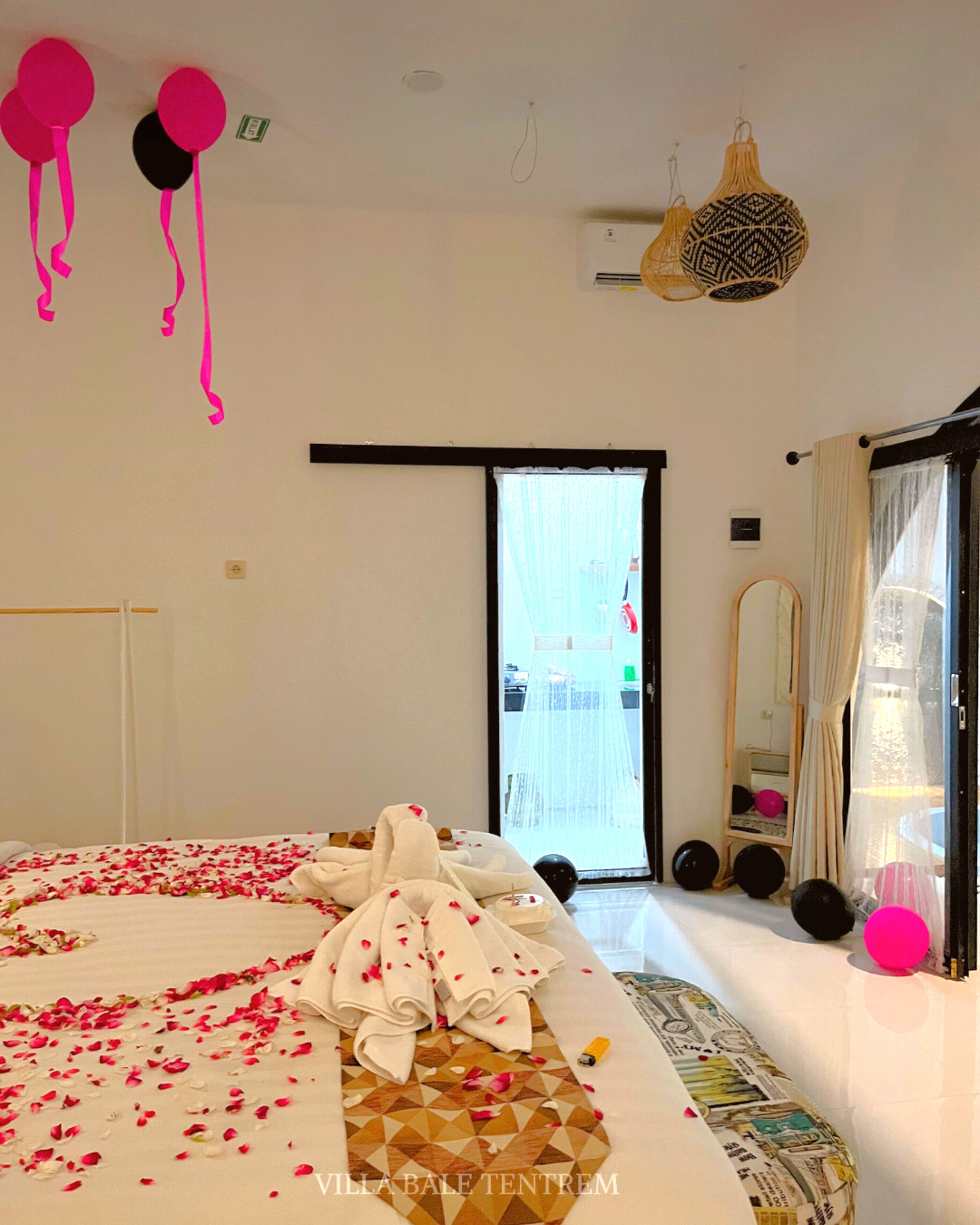 A hotel room with a bed, a large window, a mirror, and a hanging light fixture.