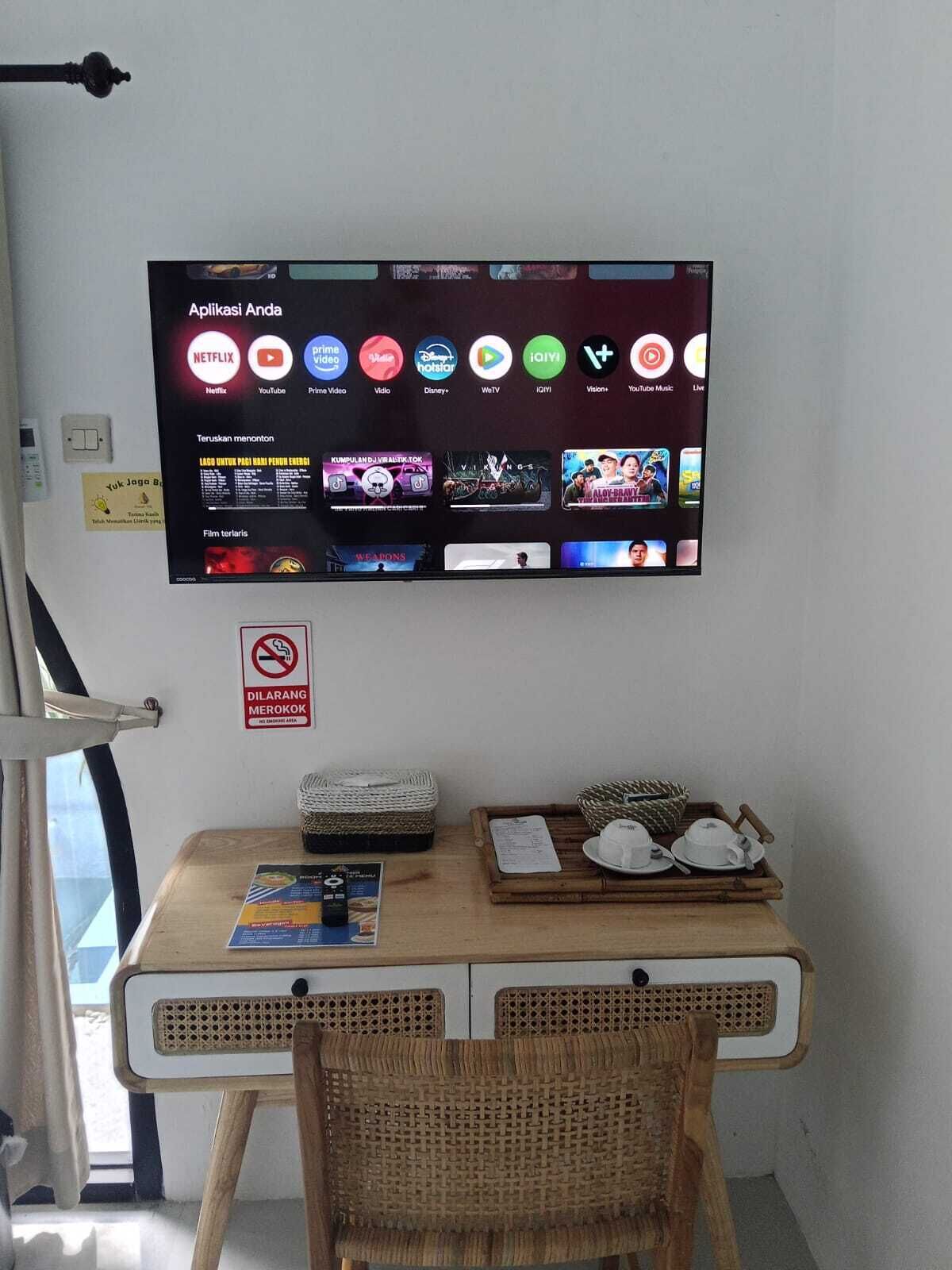 Une pièce équipée d’un téléviseur diffusant différents services de streaming, d’une table sur laquelle se trouve un plateau avec des tasses à thé, et d’un fauteuil en osier.