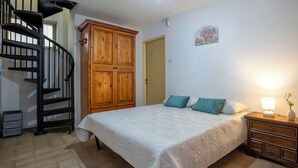 Quarto com cama, mesa de cabeceira, cômoda, armário de madeira, escada em caracol e uma porta.