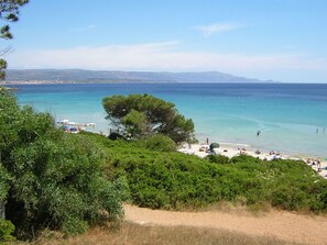 Une plage à l’eau turquoise et limpide, un rivage sablonneux, et quelques personnes profitant du soleil.