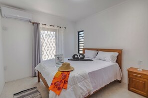 Une chambre à coucher avec un lit, une table de chevet, une fenêtre avec des stores, un rideau et un panneau accroché au mur.