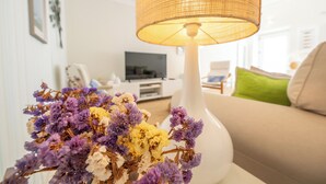 A living room with a white sofa, a white lamp, and a bouquet of flowers. - Rosemary House (Tavira)