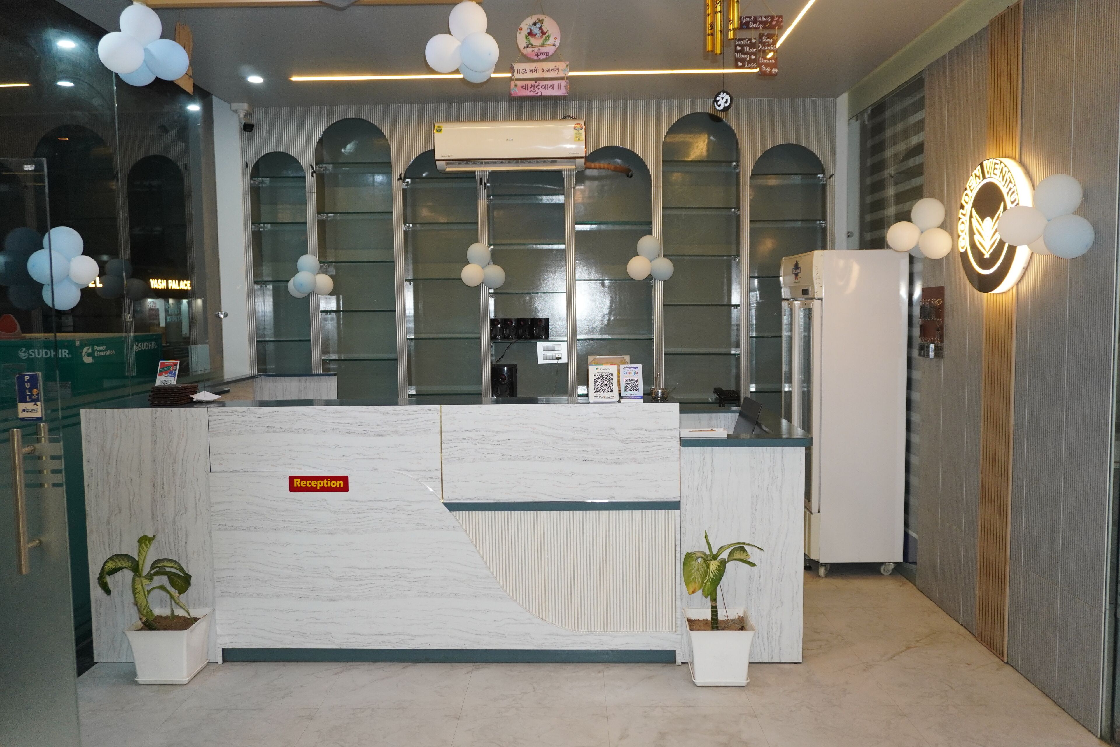 Zona de recepción con mostrador de mármol, un escritorio y un refrigerador blanco, además de un equipo de aire acondicionado instalado en la pared.