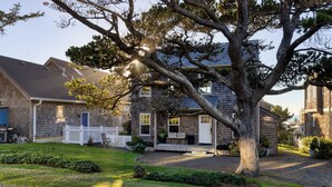 Una casa de dos pisos con un porche delantero, un árbol grande en el frente y una cerca de piquetes blancos.