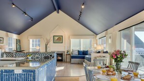 Una cocina amplia con una isla central, un comedor con mesa lista para el desayuno y un rincón acogedor con sofá y chimenea.