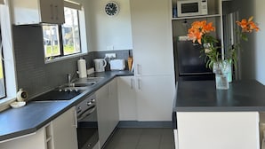 Een moderne keuken met witte kastjes, een magnetron, een spoelbak en een fornuis. Er hangt een klok aan de muur en er staat een vuilnisbak in de hoek.