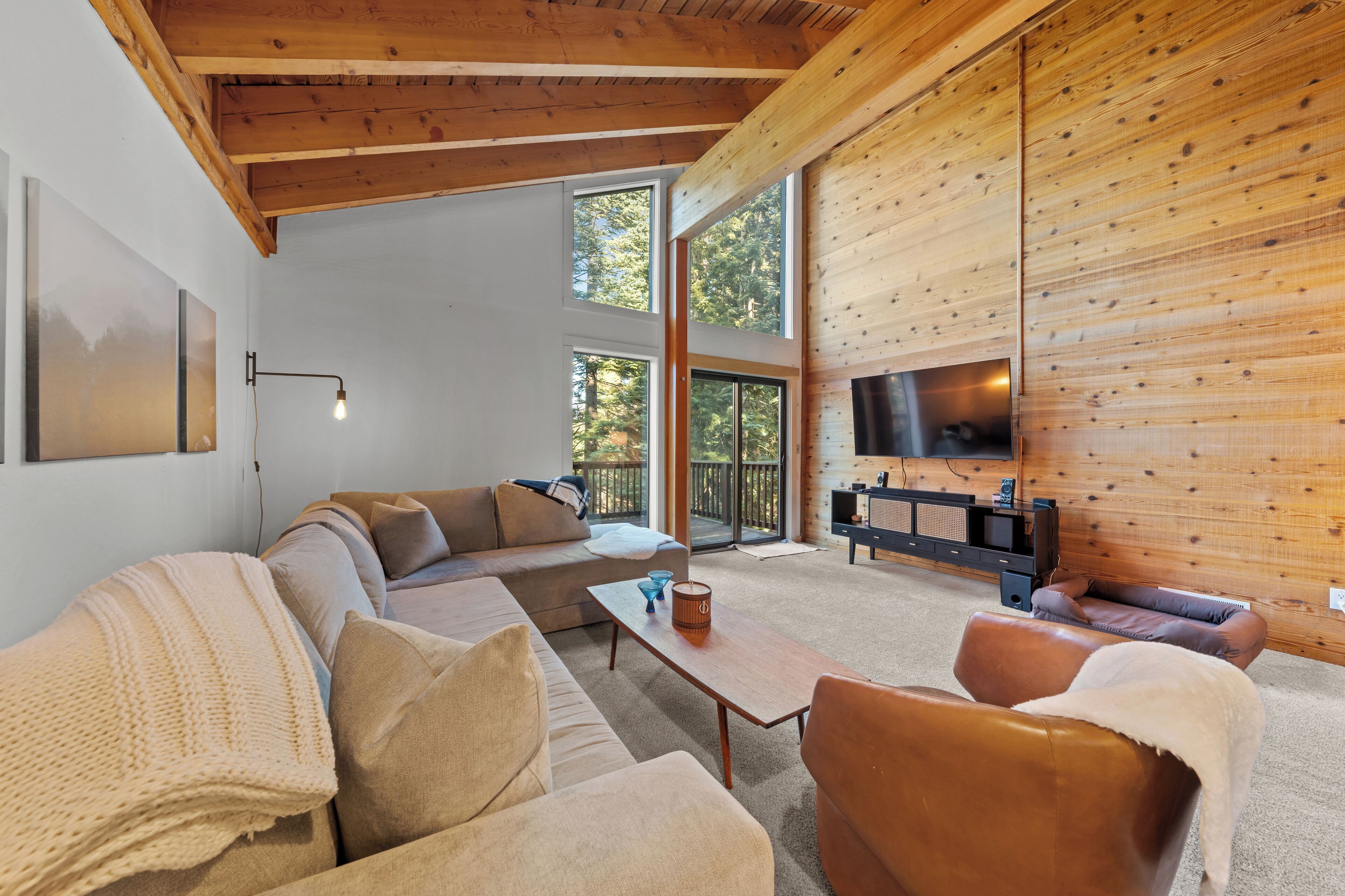 A modern living room with a sectional sofa, a coffee table, and a TV mounted on a wooden wall.
