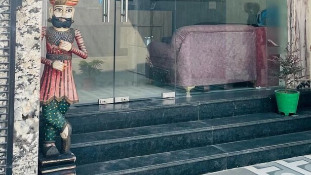 A modern building entrance with a glass door, a statue, a purple sofa, and a green potted plant. - Hotel Green Lotus (Noida)